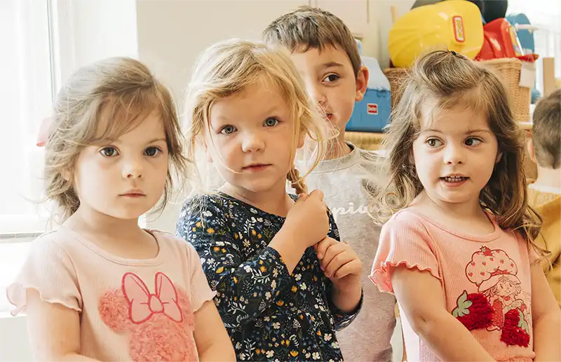 Four preschoolers standing together in a bright Head Start classroom.